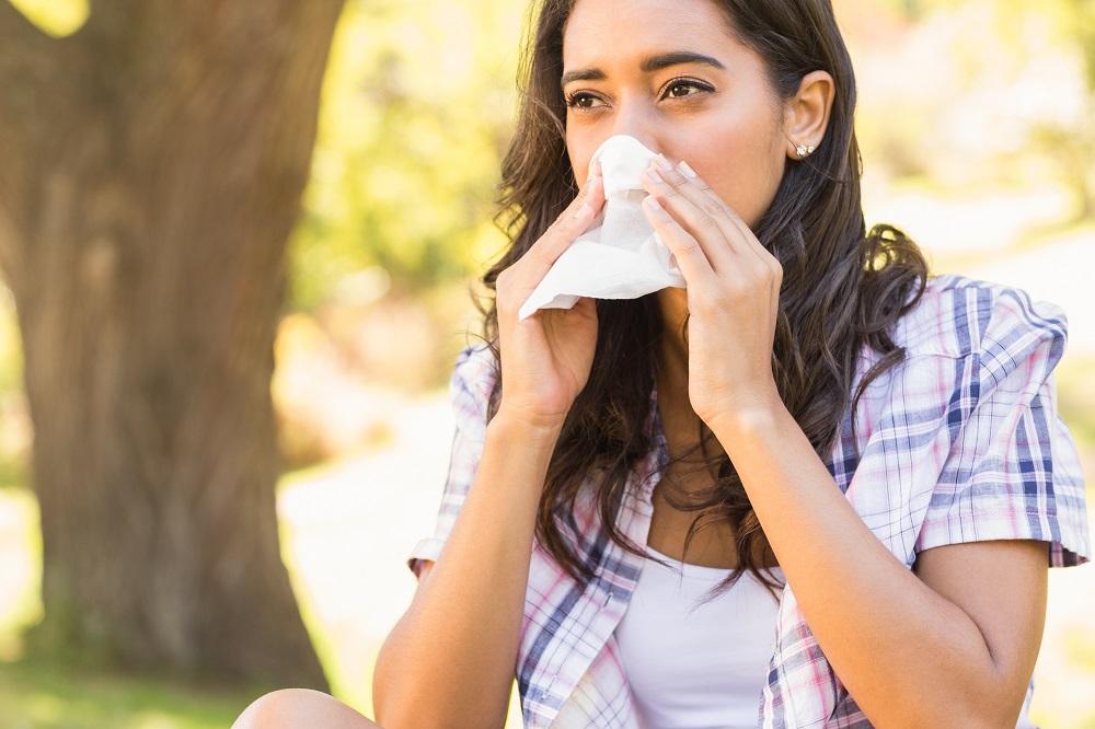 Pretty brunette blowing her nose on a sunny day